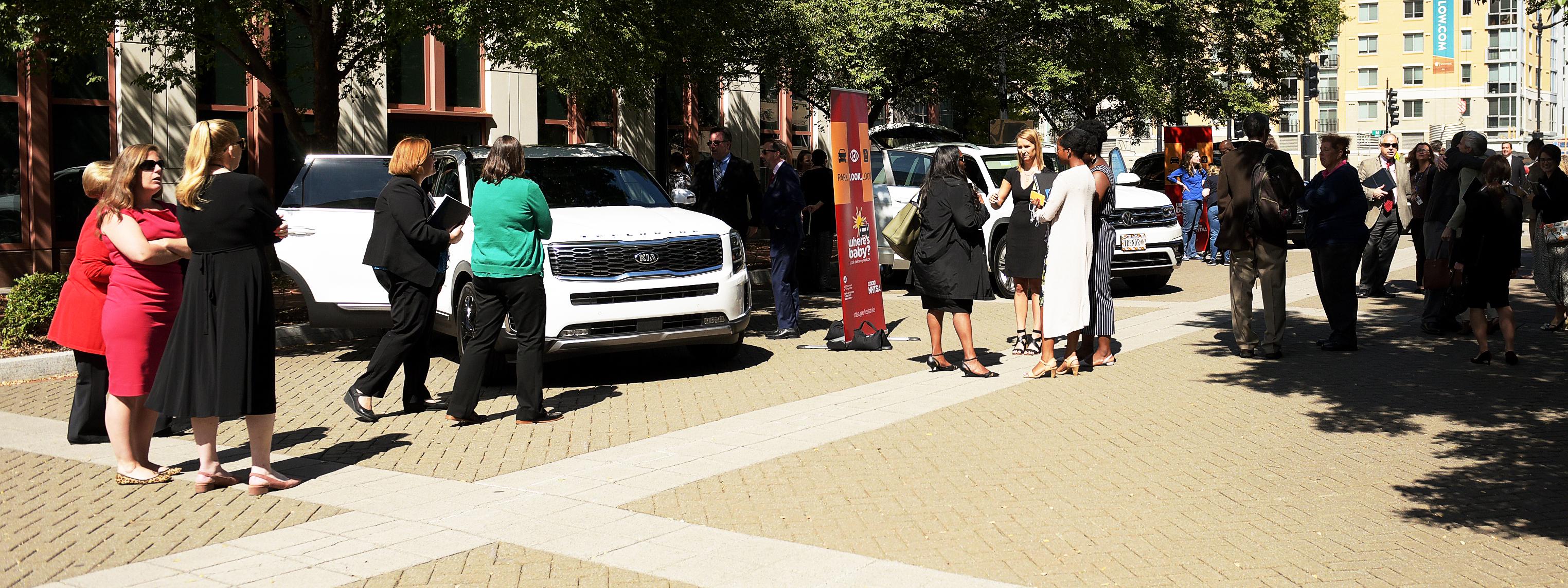 People gathered in front of cars, sign reads, park, look, lock People gathered in front of cars, sign reads, park, look, lock