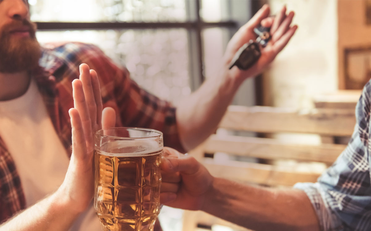 Man in bar refusing glass of beer, has keys in the other hand
