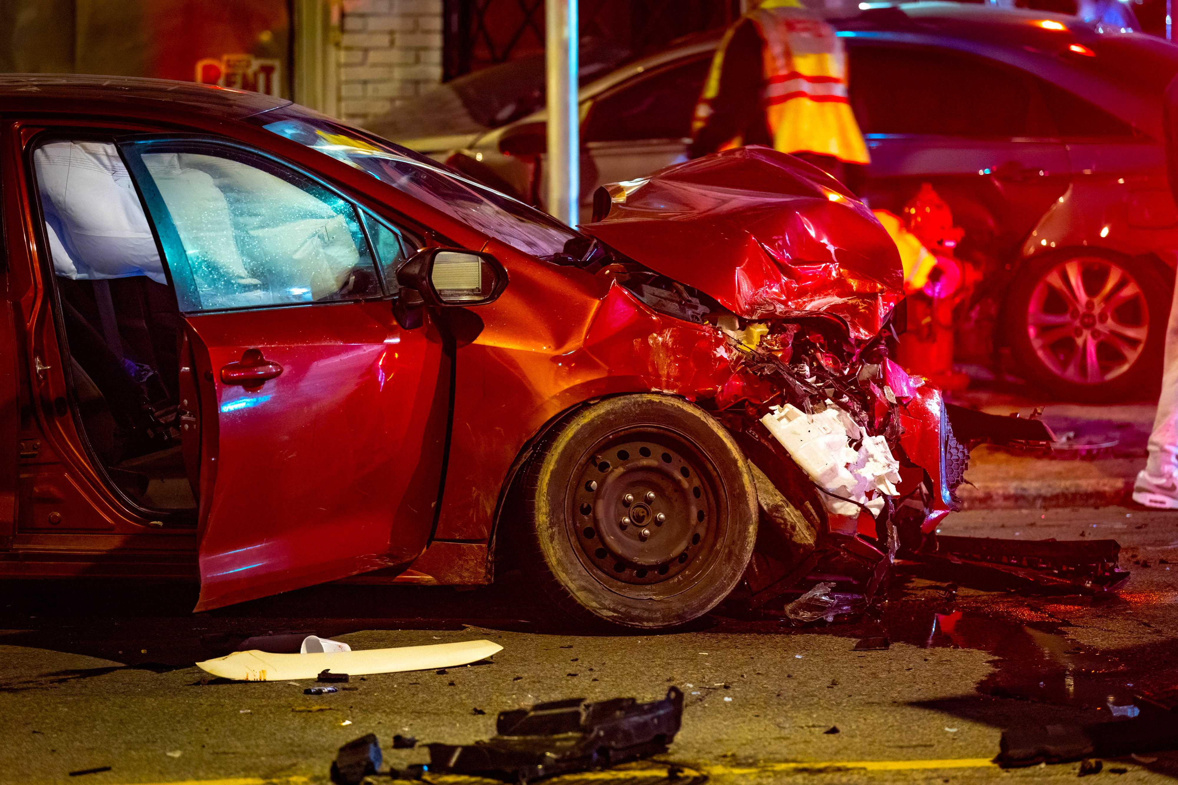 Nighttime scene showing a serious collision between two cars on a city street with visible damage, debris, and emergency atmosphere under streetlights.