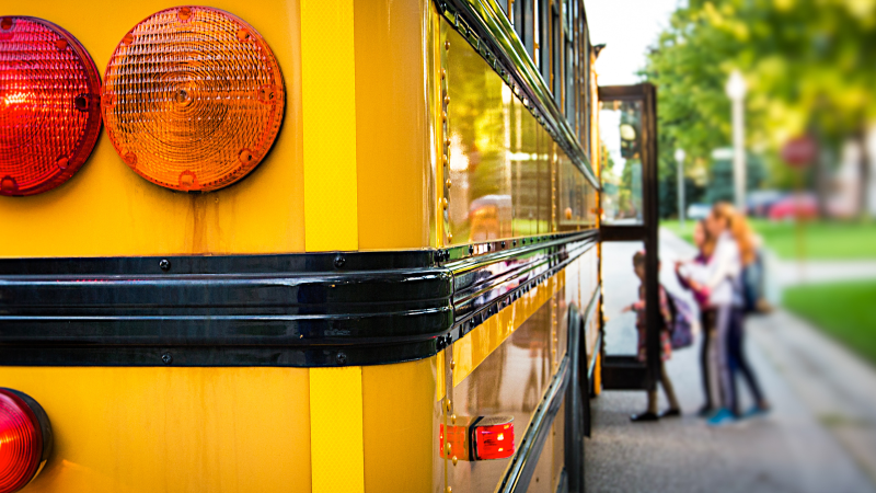 close up a school bus' tail lights with children getting on the bus in the background